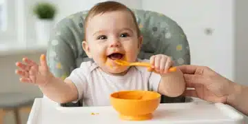 Happy baby in high chair eating first solid food, pureed sweet potato